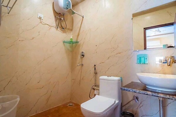 A bathroom with a marble floor, a white toilet, a glass shower enclosure, a sink, and a mirror.