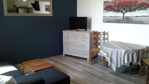 Een kamer met een houten dressoir, een televisie erop, een stoel, een tafel met een gestreepte tafelkleed en een bank.