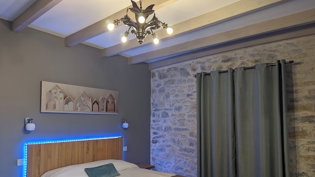 Een slaapkamer met een houten hoofdbord, een bed met wit en bruin beddengoed, een wandlamp en een stenen muur.