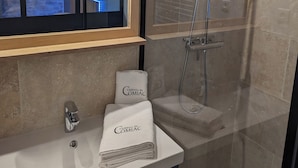 Een moderne badkamer met een douchecabine van glas, een wastafelmeubel en een raam met uitzicht op een stenen muur.