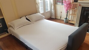 A neatly made bed with white linens, a grey upholstered headboard, and a wooden floor.