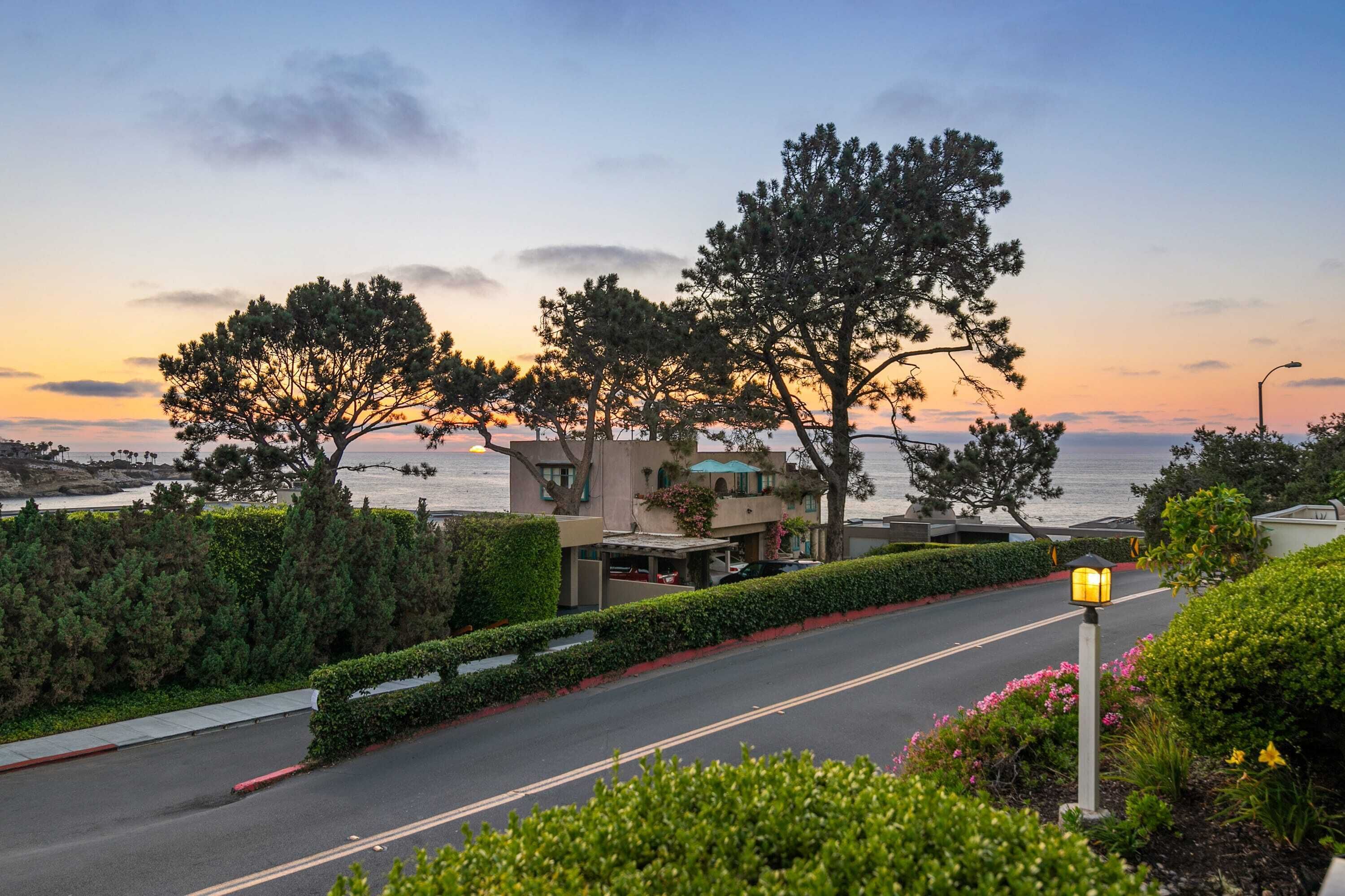 Une route côtière bordée d’un bâtiment, d’arbres et offrant une vue sur la mer.