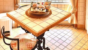 A dining area with a table set for two, a window with striped curtains, and a view of the street outside. - Delightful and spacious apartment with a view of Vesuvius - Salotto Napoletano 381 (Napoli)