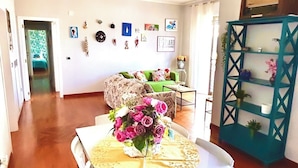 A dining area with a table set for two, a green pendant light, and a teal shelving unit with decorative items. - Delightful and spacious apartment with a view of Vesuvius - Salotto Napoletano 381 (Napoli)