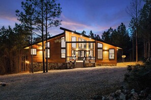 Set amidst tall pine trees, this cabin features a two-story design with a prominent entrance and stairs leading up to it.