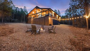 Une cabane en bois avec un foyer et des sièges d’extérieur, entourée d’arbres.