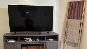 A modern living room with a flat-screen TV on a wooden stand, a fireplace, and a small table with a book.