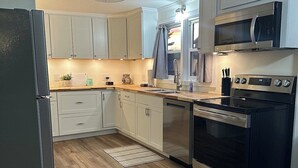 A modern kitchen with light-colored cabinets, a stainless steel refrigerator, a microwave, and an oven.