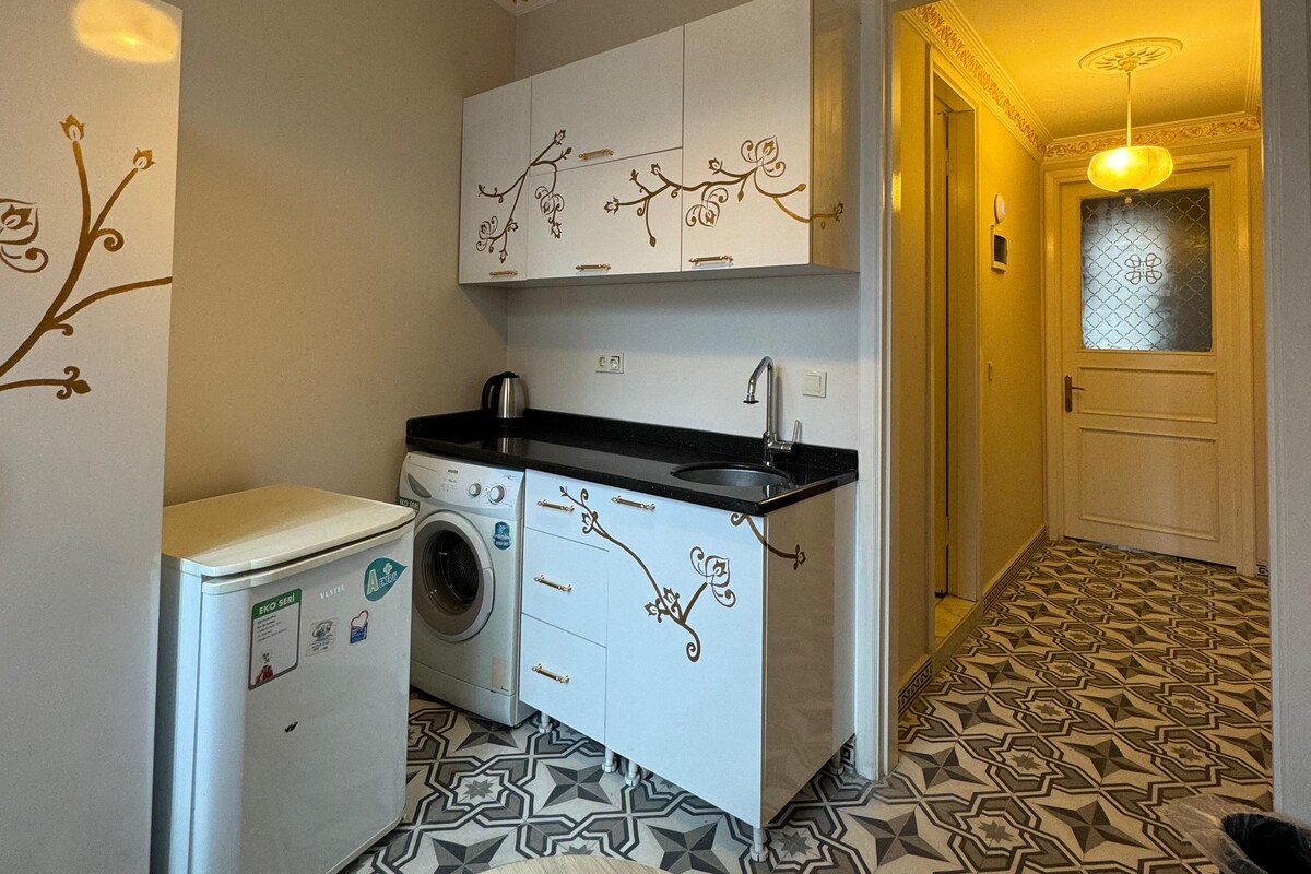 A compact kitchen with a washing machine, a sink, and decorative wall art.