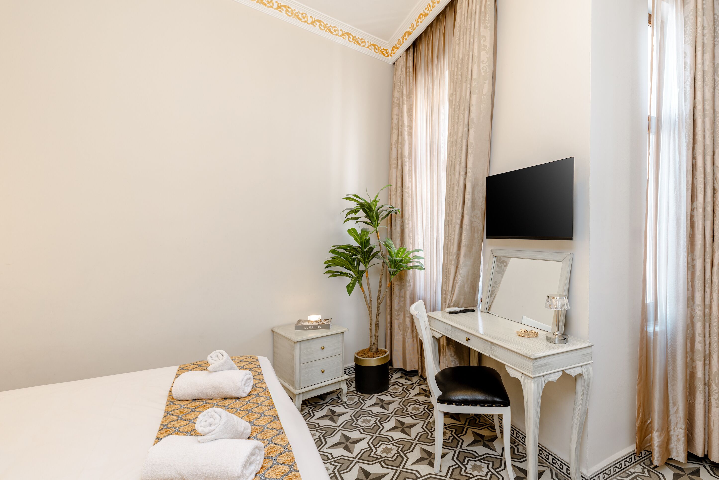 Une chambre d’hôtel avec un lit, un bureau et une chaise, une plante en pot et un téléviseur.
