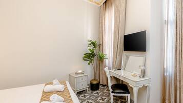 Une chambre d’hôtel avec un lit, un bureau et une chaise, une plante en pot et un téléviseur.