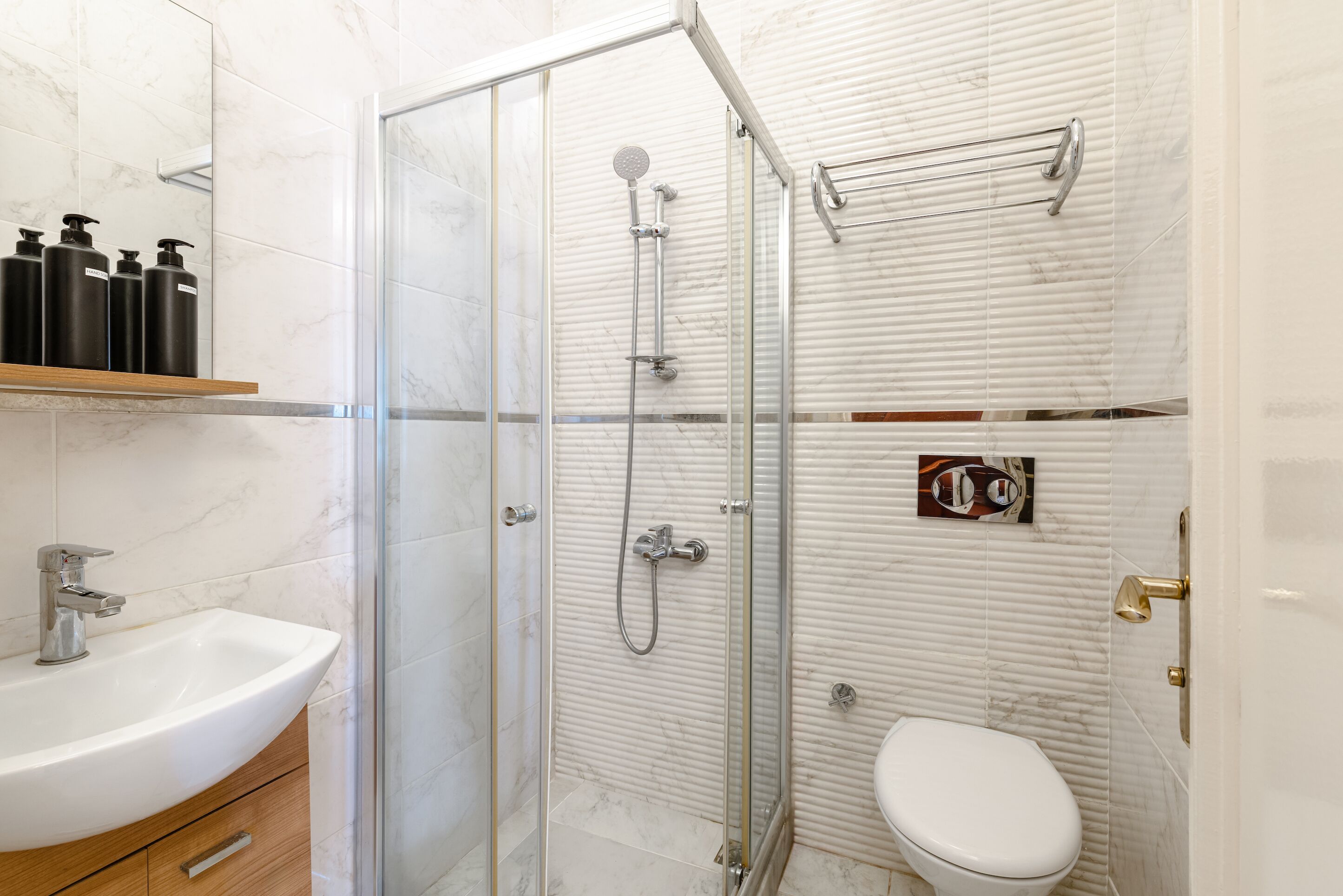 Een moderne badkamer met een douchecabine van glas, een witte wastafel en een toilet.