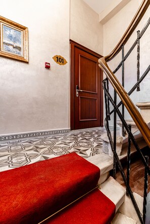 A staircase with a red carpet, a wooden door with a number plaque, and a wall-mounted fire alarm. - Felicity Palace Sirkeci (Istanbul)