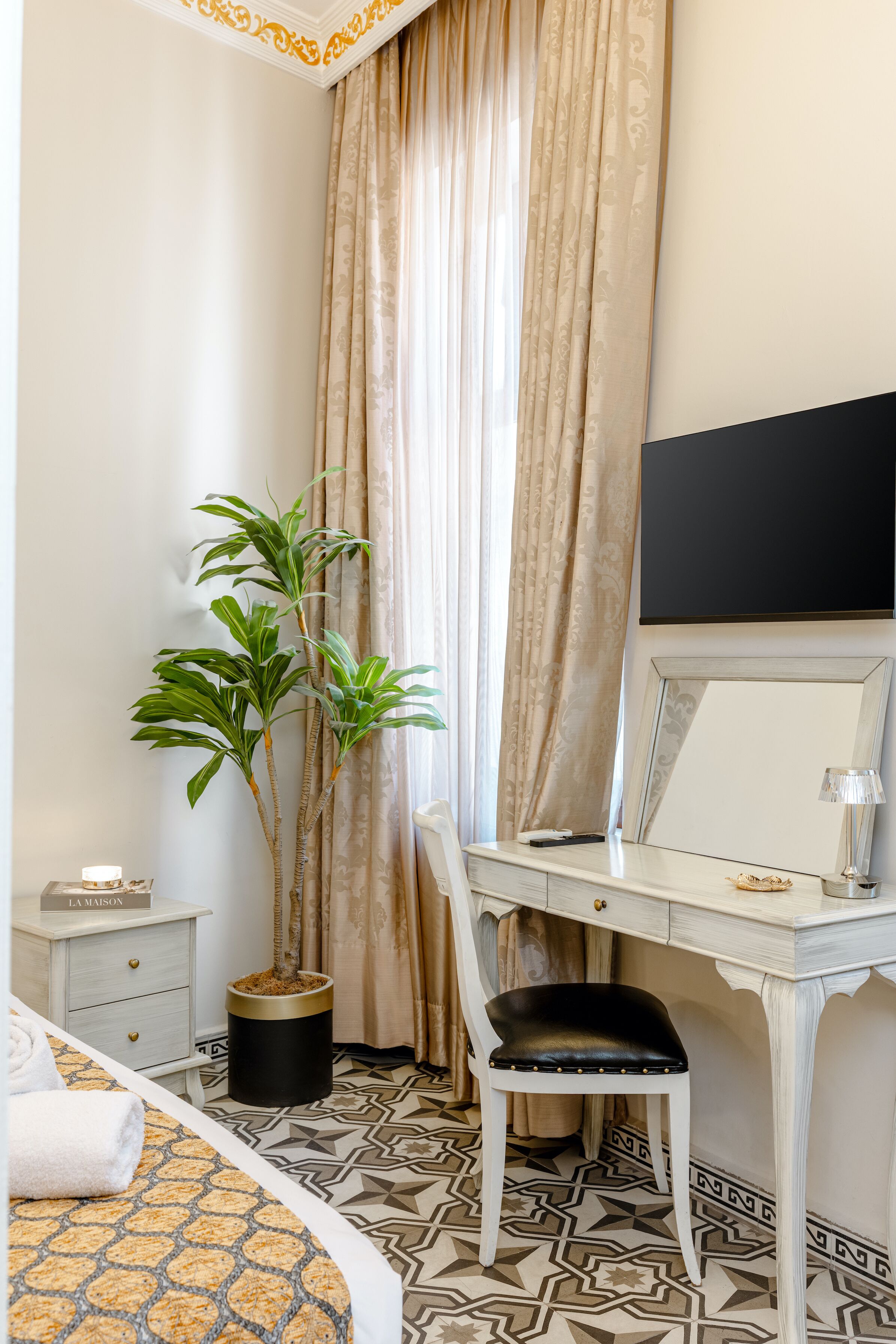 Een hotelkamer met een bed, een bureau met stoel, een potplant, een televisietoestel en een nachtkastje met lamp.