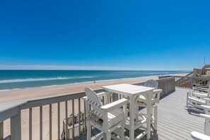 Una terraza de madera con sillas y mesas blancas con vista a la playa.