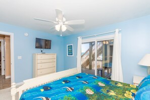Un dormitorio con cama, ventilador de techo, televisión, cómoda y vista al exterior.