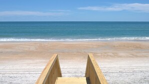 Un muelle de madera que conduce a una playa arenosa con vista despejada al océano.