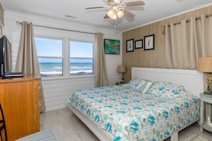 A bedroom with a bed, a desk, a chair, a window with curtains, a ceiling fan, and a wall with framed pictures. - Carolina Charm - Classic 3BR Oceanfront Cottage, Dog Friendly! (Surf City)