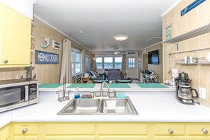 A compact kitchen with a sink, a microwave, and a coffee maker. There is a dining area with a table and chairs, and a view of the ocean through large windows.