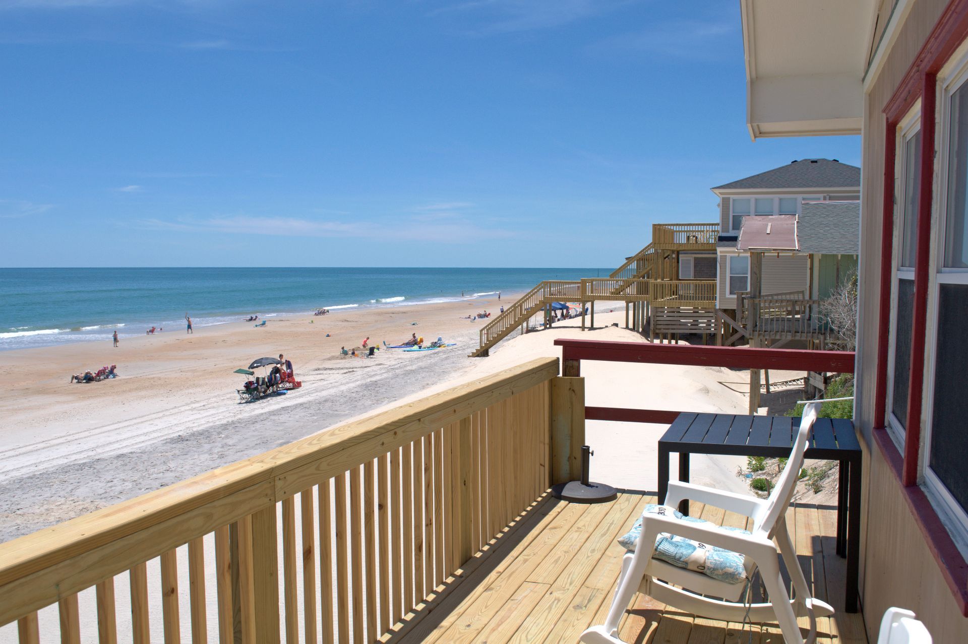 A wooden deck with a view of a beach, a building with a balcony, and a clear sky.