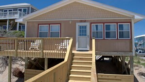 Una casa frente al mar con una terraza de madera, un porche delantero y una escalera que conduce a la entrada.
