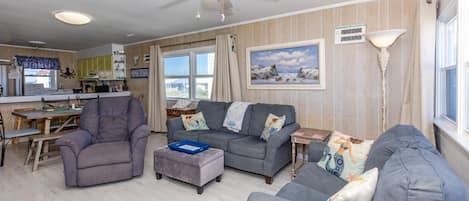 A living room with a dining area, a ceiling fan, a painting, and a lamp.