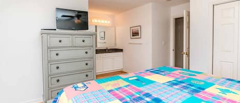 A bedroom with a bed, dresser, television, and a door.