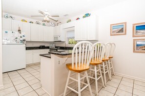 A kitchen with white cabinets, a microwave, a ceiling fan, and three white bar stools. - Almost Beachfront - Cozy 2nd Row Home with 4 Bedrooms (Surf City)