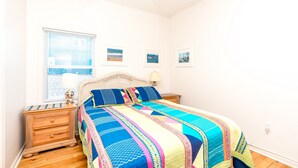 A bedroom with a bed, a nightstand, a dresser, a window with blinds, and three framed pictures on the wall. - Almost Beachfront - Cozy 2nd Row Home with 4 Bedrooms (Surf City)