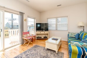 A living room with a television, a sofa, a chair, a small table, and a window. - Almost Beachfront - Cozy 2nd Row Home with 4 Bedrooms (Surf City)