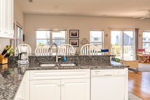 A kitchen with a granite countertop, white cabinets, a built-in dishwasher, and a window overlooking a deck. - Almost Beachfront - Cozy 2nd Row Home with 4 Bedrooms (Surf City)