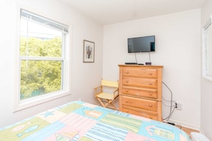 A bedroom with a bed, a wooden dresser, a television on the wall, and a window with a view of trees. - Almost Beachfront - Cozy 2nd Row Home with 4 Bedrooms (Surf City)
