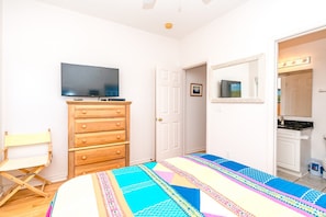 A bedroom with a bed, a wooden dresser, a television, a door, and a bathroom visible through an open door. - Almost Beachfront - Cozy 2nd Row Home with 4 Bedrooms (Surf City)