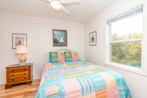 A bedroom with a bed, a nightstand, a lamp, and a window. - Almost Beachfront - Cozy 2nd Row Home with 4 Bedrooms (Surf City)