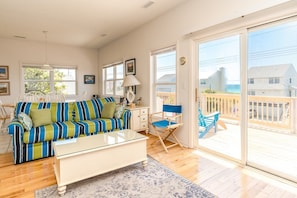 A bright living room with a striped sofa, a coffee table, and a view of the deck. - Almost Beachfront - Cozy 2nd Row Home with 4 Bedrooms (Surf City)