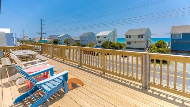 A wooden deck with outdoor furniture, overlooking a residential area with houses and a clear blue sky. - Almost Beachfront - Cozy 2nd Row Home with 4 Bedrooms (Surf City)
