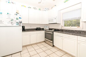 Una cocina con armarios blancos, microondas, estufa y refrigerador.