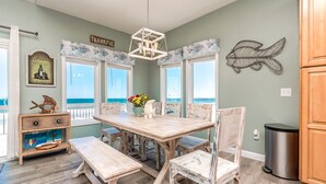 A dining area with a wooden table and chairs, a chandelier, and a view of the ocean.