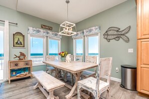Un comedor con mesa y sillas de madera, una araña y vista al océano.