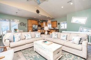 Ein Wohnzimmer mit einem Ecksofa, einem Couchtisch und einer Küche im Hintergrund.