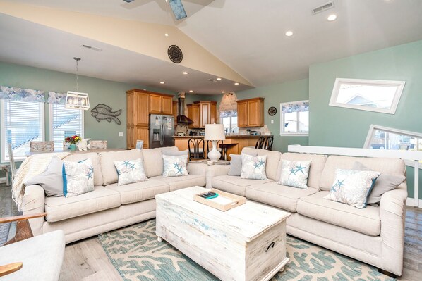 A living room with a sectional sofa, a coffee table, and a kitchen in the background.