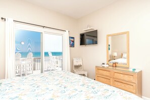 A bedroom with a bed, a dresser, a mirror, a television, and a view of the sea through a sliding door.