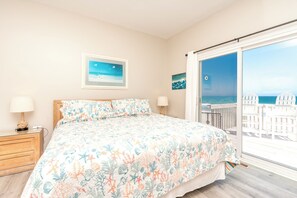 A bedroom with a bed, nightstands, a window with a view of the sea, and a painting on the wall.