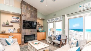 A living room with a fireplace, television, and a view of the ocean.