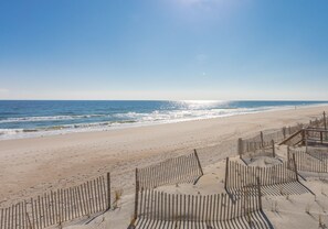 Une plage avec une clôture en bois au premier plan, un ciel dégagé et l’océan en arrière-plan.