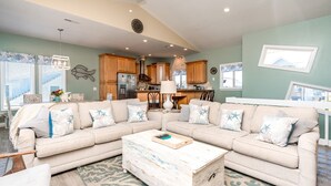 A living room with a sectional sofa, a coffee table, and a kitchen in the background.