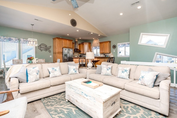 A living room with a sectional sofa, a coffee table, and a kitchen in the background.