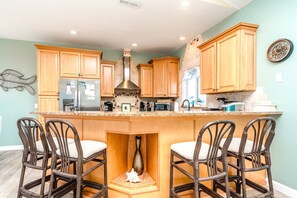 Una cocina con armarios de madera, una isla central con taburetes de bar, una campana extractora de acero inoxidable y un reloj de pared decorativo.