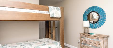 A bunk bed with a nautical-themed bedspread, a dresser with a compass design, and a round mirror with a blue and white pattern.