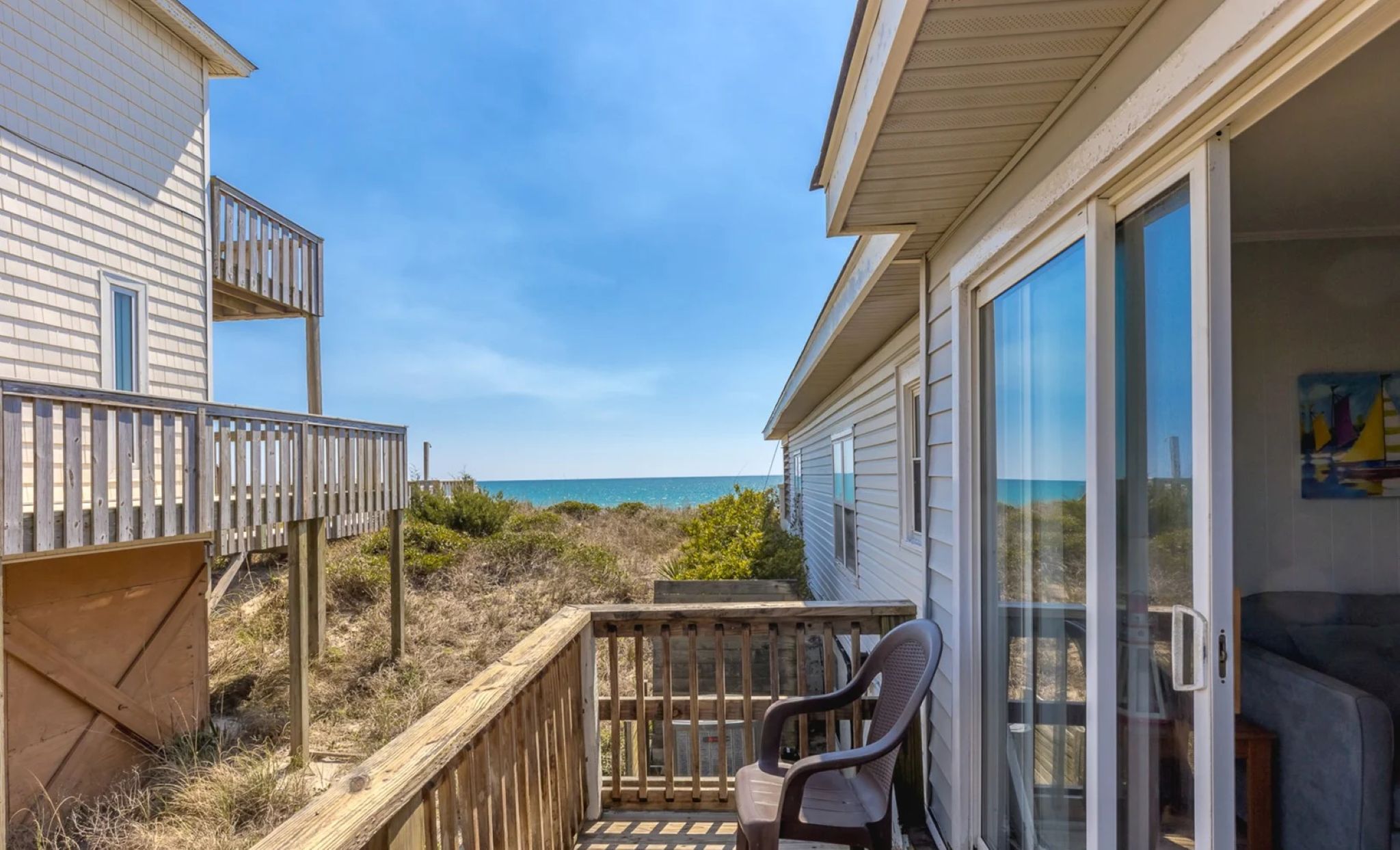 A wooden deck with a chair, a glass door leading to a room, and a view of the ocean.